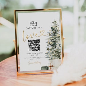 May include: A gold framed sign with a white background and a watercolour illustration of a Christmas tree. The sign says "Capture the love" with a heart and a QR code. The text below the QR code says "Share your photos with us. Scan the code with your smartphone and upload your photos. Sarah & Anthony"