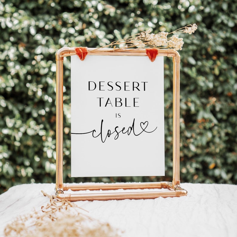 May include: A white sign with black text that reads "Dessert Table is closed" with a small heart symbol. The sign is displayed on a copper pipe stand.