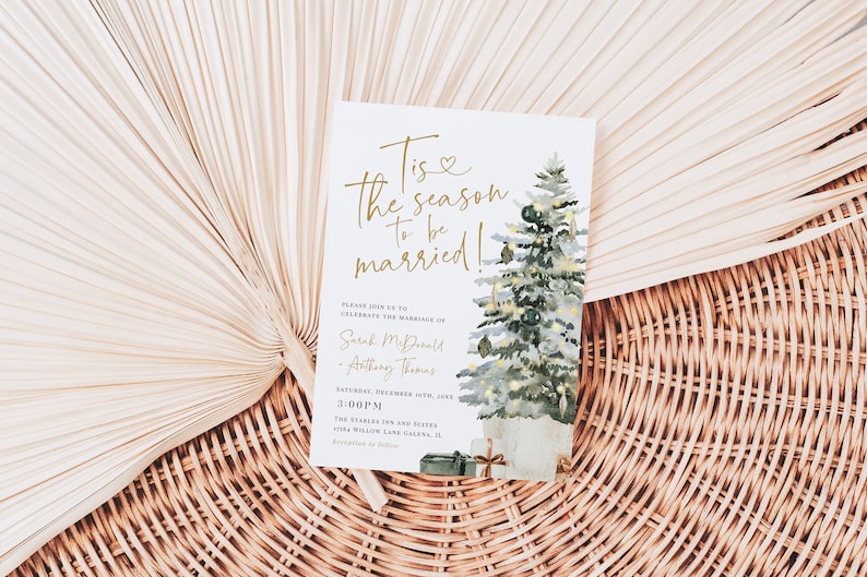 May include: A white wedding invitation with gold lettering that reads "Tis the season to be married!"  The invitation features a watercolor illustration of a Christmas tree with ornaments and presents. The text also includes the names "Sarah McDonald" and "Anthony Thomas" and the date "December 10th, 20XX".