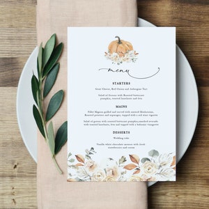 May include: A fall-themed wedding menu with a watercolor illustration of a pumpkin and floral accents. The menu lists starters, mains, and desserts. The text reads: "STARTERS Goat Cheese, Red Onion and Aubergine Tart Salad of Greens with Roasted butternut pumpkin, toasted hazelnuts and feta MAINS Fillet Mignon grilled and served with sauteed Mushrooms, Roasted potatoes and asparagus, topped with a red wine vignette Salad of greens with roasted butternut pumpkin, smashed avocado with toasted hazelnuts, fets and topped with a balsamic vinagrette DESSERTS Wedding cake Vanilla white chocolate mousse with fresh strawberries and cream"