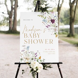 May include: A white sign with a floral design and gold lettering announcing a baby shower for Madison. The text reads "Welcome to Madison's Baby Shower 05.03.20xx 35 days until she says I Do!"