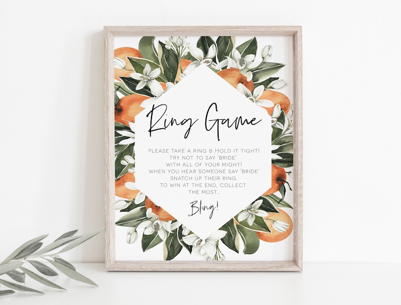 Puede incluir: Un cartel imprimible con un dise&ntilde;o floral con flores de azahar y naranjas. El cartel dice "Ring Game" e incluye instrucciones para un juego en el que los invitados intentan recoger anillos. El texto dice: "&iexcl;Por favor, toma un anillo y suj&eacute;talo bien fuerte! &iexcl;Intenta no decir 'novia' con todas tus fuerzas! Cuando escuches a alguien decir 'novia', arreb&aacute;tale su anillo. Para ganar al final, recoge la mayor cantidad... &iexcl;Bling!"