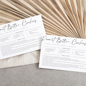 May include: Two printable recipe cards for peanut butter cookies. The cards are white with black text and include the ingredients and directions for making the cookies. The cards are laid out on a light brown surface.