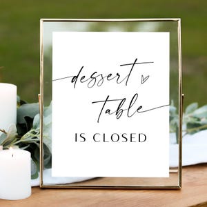 May include: A white sign in a gold frame with black calligraphy that reads "dessert table is closed" with a small heart symbol.