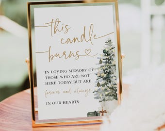 May include: A white sign with gold lettering in a gold frame reads "This candle burns in loving memory of those who are not here today but are forever and always in our hearts". A watercolor painting of a Christmas tree with lights and presents is on the right side of the sign.