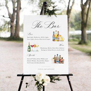 May include: A white sign with black calligraphy that reads "The Bar" and lists the beer, wine, and spirits available at the bar. The sign is on an easel with white flowers.