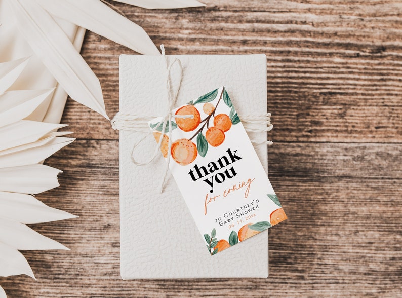 May include: A white gift box with a brown twine bow and a thank you tag with orange citrus fruit illustrations. The tag says "thank you for coming to Courtney's Baby Shower 06.11.20xx".