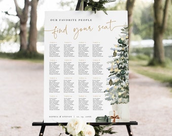 May include: A white wedding seating chart with a watercolor illustration of a Christmas tree with lights and presents. The chart is titled "Our Favorite People Find Your Seat" and lists the names of guests at each table. The chart is on a black easel.