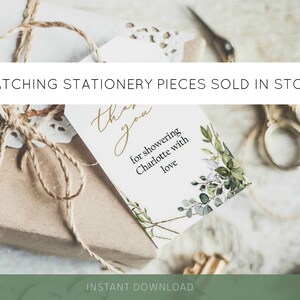 May include: A wrapped gift with a tag that reads "Thank you for showering Charlotte with love." The tag is decorated with green foliage and gold accents. The text "Matching Stationery Pieces Sold in Store" is at the top.