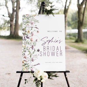 May include: A white sign with a floral border and the text "Welcome to Sophia's Bridal Shower, Saturday, July 13th 2024". The sign is on a black easel.
