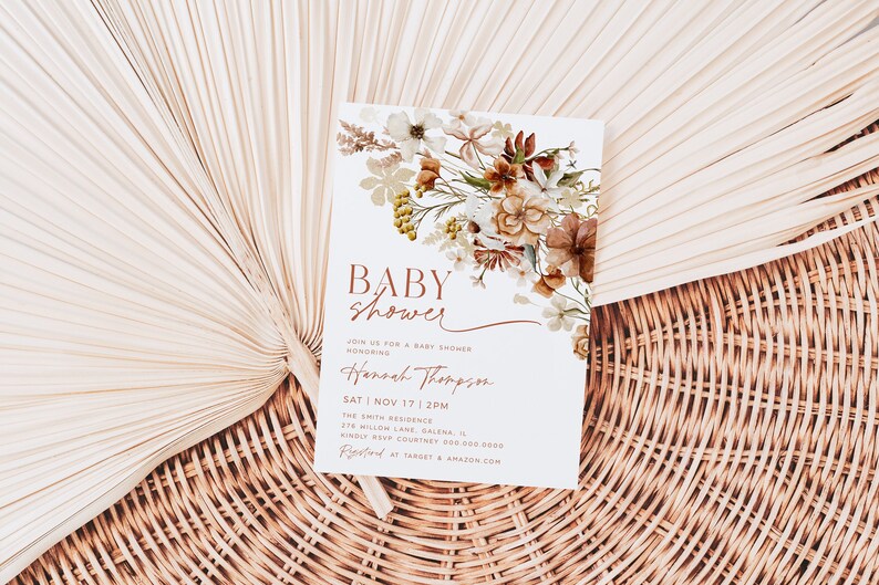 May include: A white baby shower invitation with a floral design in shades of brown and beige. The text reads "BABY SHOWER" in a brown script font. The invitation includes the date, time, and location of the shower, as well as the name of the honoree, Hannah Thompson.