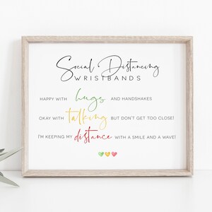 Op de afbeelding: Een ingelijste print met de woorden "Social Distancing Wristbands" in zwart script. Hieronder staat in kleurrijke tekst: "Happy with hugs and handshakes", "Okay with talking but don't get too close!" en "I'm keeping my distance with a smile and a wave!"