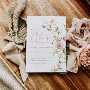 May include: A white invitation with pink watercolor flowers and the text "Our Little Wild Flower is turning one!"  Join us for a birthday celebration for Madison Lucy. Saturday, August 28th, 202X at 2:00 PM. The Hungry Lady Bug Cafe, 17564 N Willow Lane Galena, IL. RSVP Courtney Handley 555-354-3667.