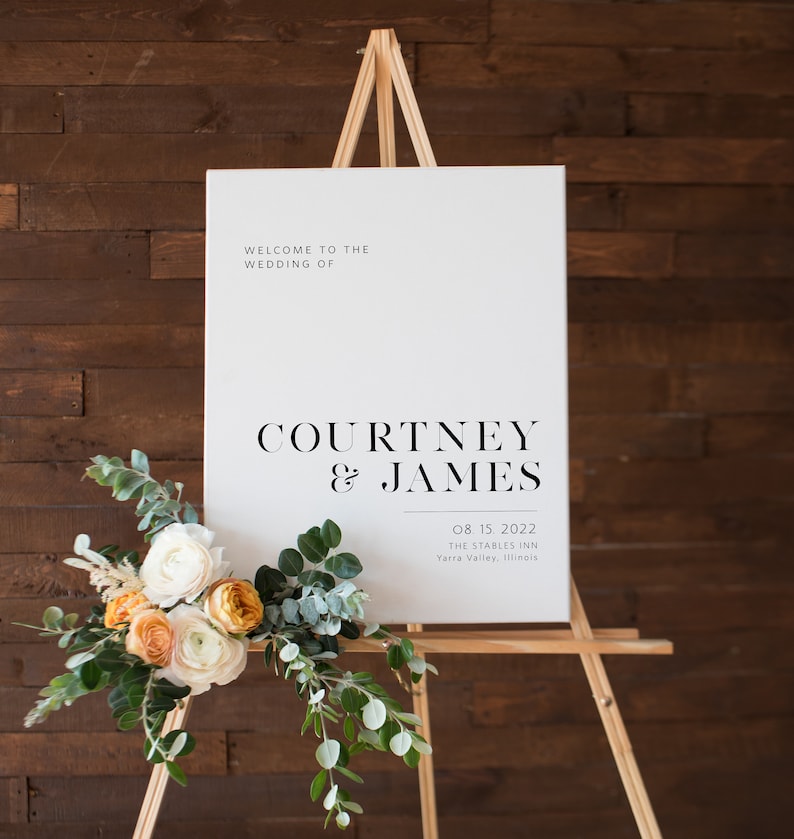 K&ouml;nnte beinhalten: Wei&szlig;es Hochzeitseingangsschild mit schwarzem Text. Das Schild lautet "Willkommen zur Hochzeit von Courtney & James 08.15.2022 The Stables Inn Yarra Valley, Illinois".