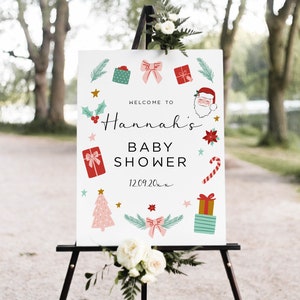 May include: A white sign with a Christmas theme announcing a baby shower for Hannah. The sign features a Santa Claus, presents, candy canes, and a Christmas tree. The date of the shower is 12.09.20.