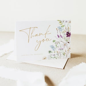May include: A white thank you card with gold lettering that says "Thank you" and "with love, The McDonalds". The card has a floral design on the right side with purple, blue, and white flowers.
