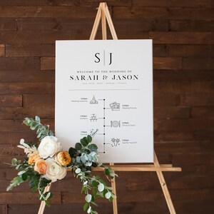 May include: A white wedding sign with a black easel stand. The sign has the initials "SJ" at the top and the text "Welcome to the wedding of Sarah & Jason" with the date "July 24th, 2022" and location "Galena, Illinois". The sign also has a timeline of wedding events with icons and times.