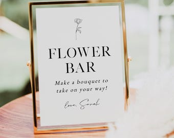 May include: A gold-framed sign with the words "FLOWER BAR" in bold black letters. Below, the text reads, "Make a bouquet to take on your way!" and "love, Sarah." A small floral illustration is at the top.