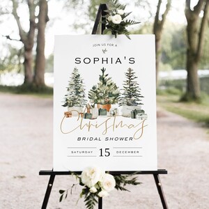 Puede incluir: Un cartel blanco con texto dorado anunciando una despedida de soltera navide&ntilde;a para Sophia el s&aacute;bado 15 de diciembre. El cartel presenta una ilustraci&oacute;n de acuarela de tres &aacute;rboles de Navidad decorados.