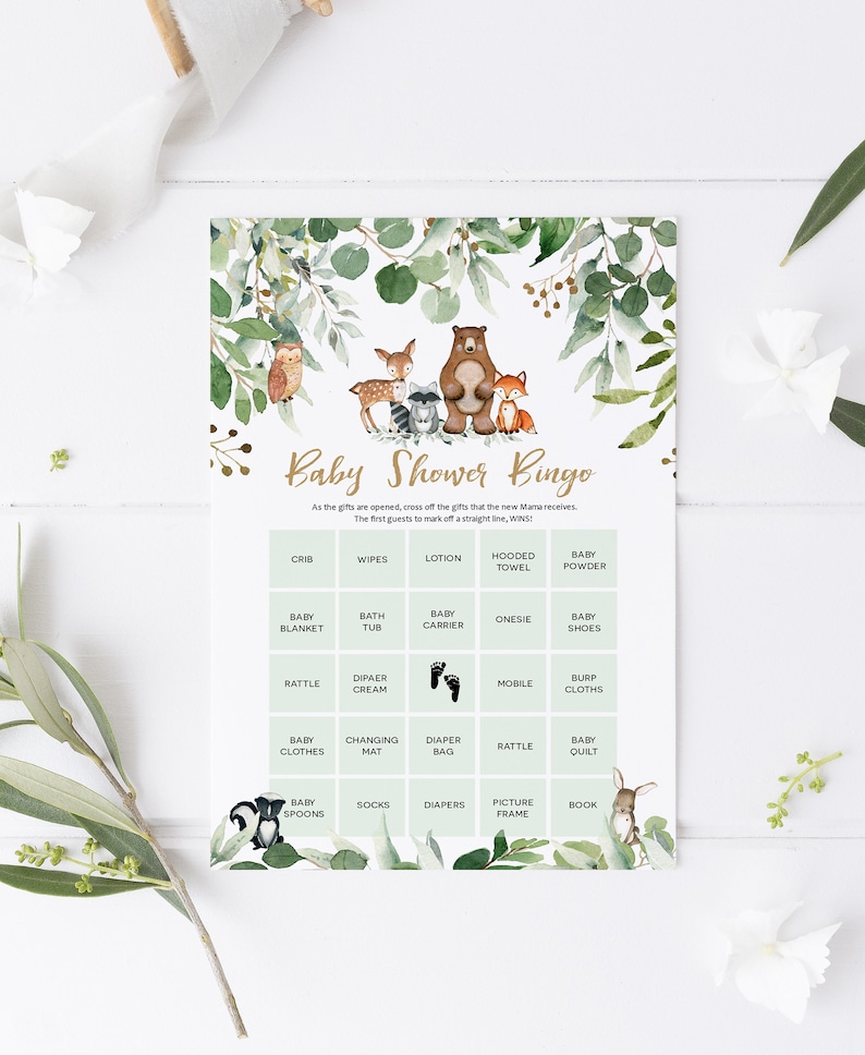 May include: A green and gold baby shower bingo card with woodland animal illustrations. The card has a grid of 25 squares with various baby items listed in each square. The text at the top reads "Baby Shower Bingo".
