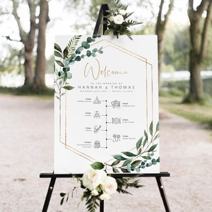 May include: A white wedding welcome sign with a gold geometric frame and green foliage. The sign includes the names Hannah & Thomas and the wedding date September 24th, 2022. The sign also includes a timeline of wedding events.
