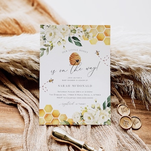 May include: A white and gold baby shower invitation with a honeycomb pattern and a bee illustration. The text reads "Our little honey is on the way!" and includes the name "Sarah McDonald" and details for the event.