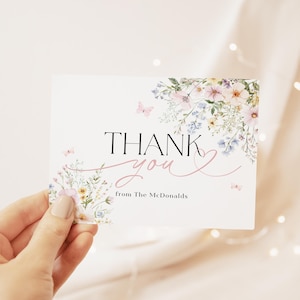 以下が含まれることがあります： ピンク、ブルー、イエローの色の花柄が描かれた白いサンキューカード。カードには黒い筆記体で「ありがとう」とピンクのハート、黒いテキストで「マクドナルドより」と書かれている。