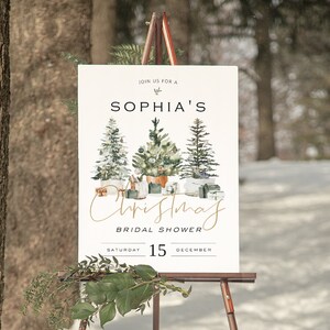 Puede incluir: Un cartel blanco con letras doradas anunciando la despedida de soltera navide&ntilde;a de Sophia para el s&aacute;bado 15 de diciembre. El cartel presenta una ilustraci&oacute;n de acuarela de tres &aacute;rboles de Navidad con regalos debajo.