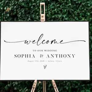 May include: White wedding welcome sign with black text that reads "welcome to our wedding Sophia & Anthony August 17th, 2028 Galena, Illinois" with a small heart symbol at the bottom.