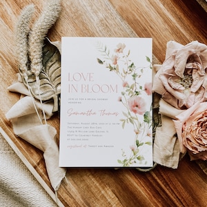 May include: A bridal shower invitation with a floral design. The invitation reads "Love in Bloom" and includes the bride's name, Samantha Thomas, the date and time of the shower, the location, and RSVP information. The invitation also includes the text "registered at Target and Amazon".