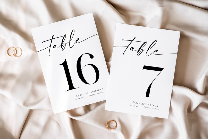 May include: Two white table number cards with black calligraphy. The top card says "Table 16" and the bottom card says "Table 7". Both cards have the text "Sarah and Anthony" and the date "10.16.2021" in smaller font.