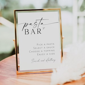 May include: A gold-framed sign with the text "pasta BAR" in black script font. The sign also includes instructions for a pasta bar: "Pick a pasta, select a sauce, choose a topping, enjoy a side." The sign is signed "Sarah and Anthony."