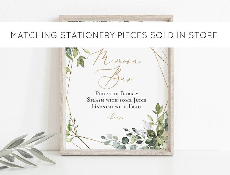 May include: A framed sign with the words "Mimosa Bar" in elegant gold script. The sign includes instructions: "Pour the Bubbly, Splash with some Juice, Garnish with Fruit." Greenery and gold geometric accents frame the text. The text "Matching Stationery Pieces Sold in Store" is at the top.