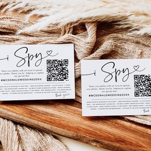 May include: Two white cards with black text and a QR code. The text reads "i Spy" and "Share your photos with us! Scan to upload your photos. Thank you for helping us capture our special day! #MCDONALDWEDDING20XX".