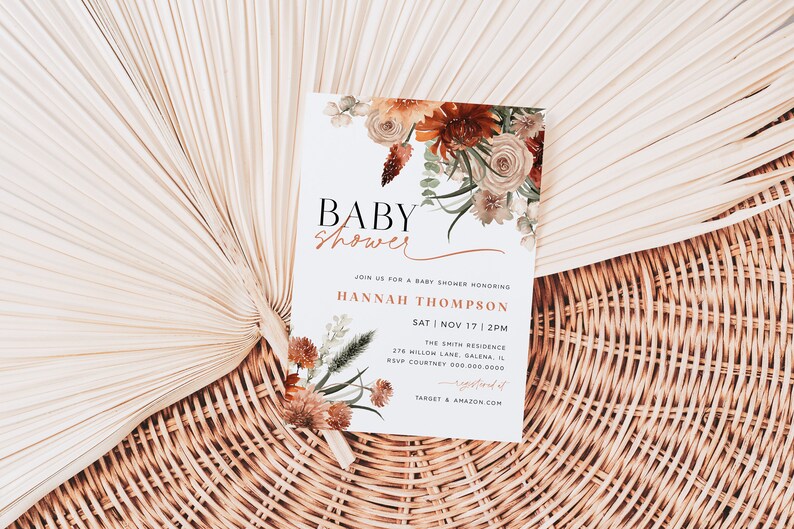 May include: A white baby shower invitation with a floral design in shades of orange, brown, and white. The text reads "Baby Shower" in a black and white font, followed by "Join us for a baby shower honoring Hannah Thompson" in a brown font. The date and time of the shower are listed as "Sat | Nov 17 | 2PM". The location is listed as "The Smith Residence, 276 Willow Lane, Galena, IL". The RSVP information is listed as "RSVP Courtney 000-000-0000". The bottom of the invitation reads "Target & Amazon.com".