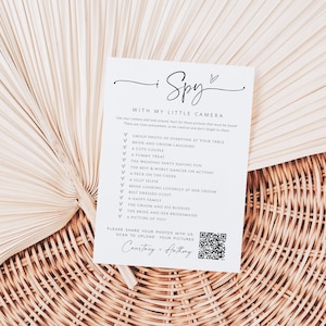 May include: A white card with the text "I Spy with my little camera" and a list of things to find at a wedding. The card also includes a QR code with the text "Please share your photos with us. Scan to upload your pictures. Courtney + Anthony."