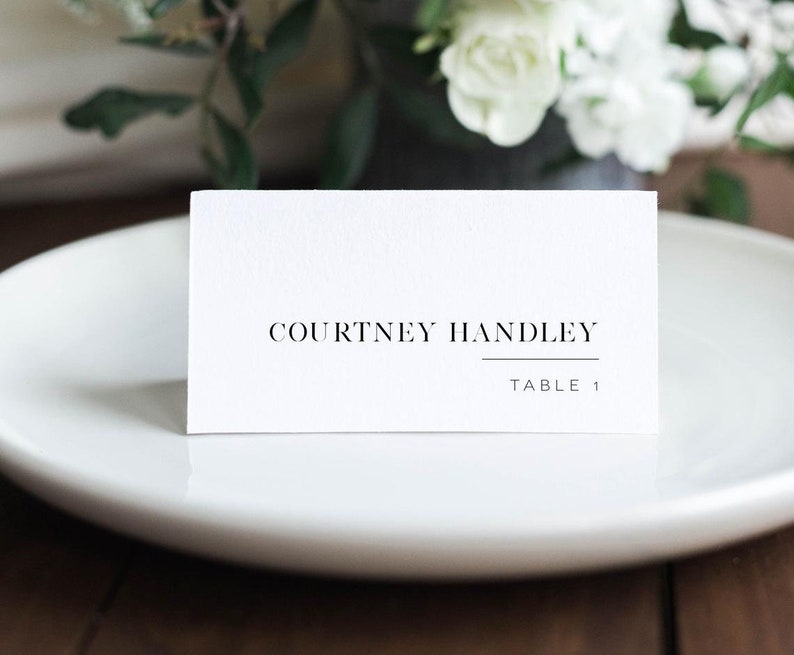 K&ouml;nnte beinhalten: Wei&szlig;e Tischkarte mit schwarzem Text "Courtney Handley" und "Tisch 1".