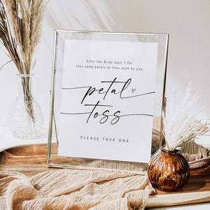 May include: A white sign with black text in a gold frame that says "After the Bride says 'I Do', toss some petals as they walk by you. Petal Toss. Please take one."