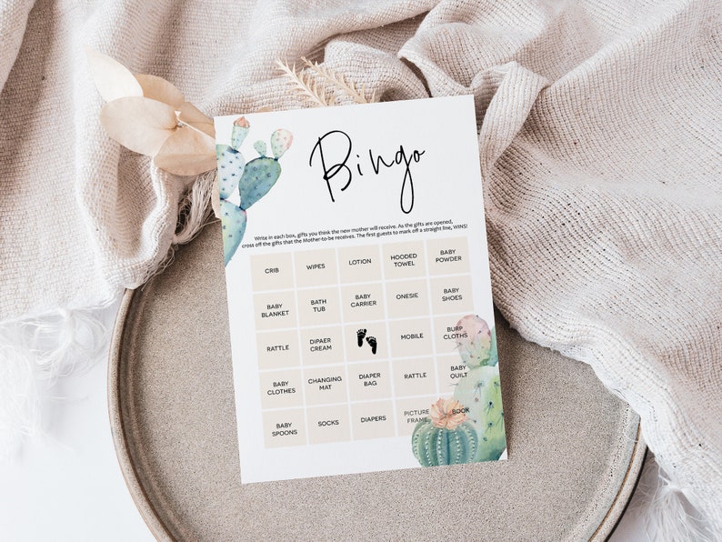 Puede incluir: Una tarjeta de bingo para baby shower imprimible con una ilustraci&oacute;n de cactus. La tarjeta tiene una cuadr&iacute;cula con casillas que incluyen art&iacute;culos que se suelen regalar en las baby showers, como pa&ntilde;ales, toallitas y una toalla con capucha. El texto "Bingo" est&aacute; en la parte superior de la tarjeta.