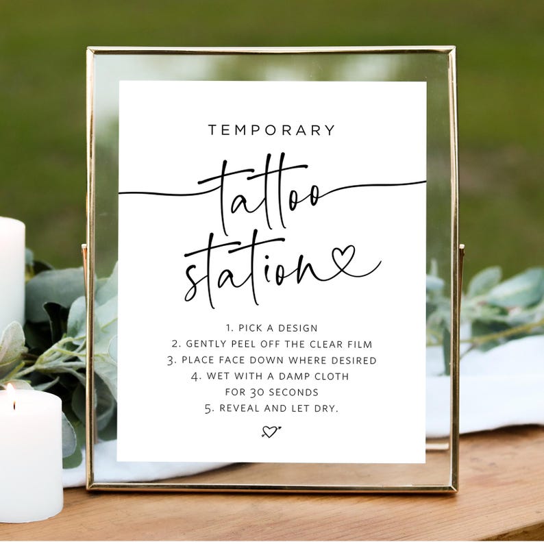 May include: A white sign with black text that reads "TEMPORARY tattoo station" with a heart symbol. The sign also includes instructions on how to apply temporary tattoos.