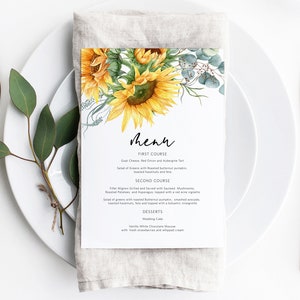 K&ouml;nnte beinhalten: Eine Sonnenblumen-Hochzeitskarte mit einer Aquarell-Illustration von Sonnenblumen und Eukalyptusbl&auml;ttern. Das Men&uuml; listet den ersten Gang, den zweiten Gang und die Desserts auf. Der erste Gang ist Ziegenk&auml;se-, Rotzwiebel- und Auberginentarte. Der zweite Gang ist gegrilltes Filet Mignon, serviert mit sautierten Pilzen, Bratkartoffeln und Spargel, betr&auml;ufelt mit einer Rotweinsauce. Die Desserts sind Hochzeitstorte und Vanille-Wei&szlig;schokoladenmousse mit frischen Erdbeeren und Schlagsahne.