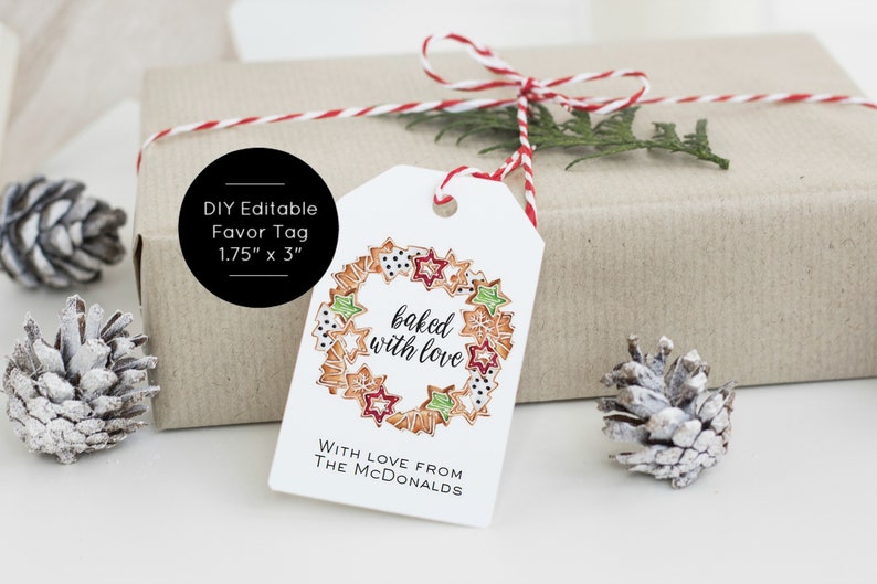 May include: White gift tag with a red and white twine bow. The tag features a wreath of gingerbread cookies with red, green, and white icing. The text "baked with love" is written in black cursive. The text "WITH LOVE FROM THE MCDONALDS" is written in black below the wreath. The tag is 1.75 inches by 3 inches.