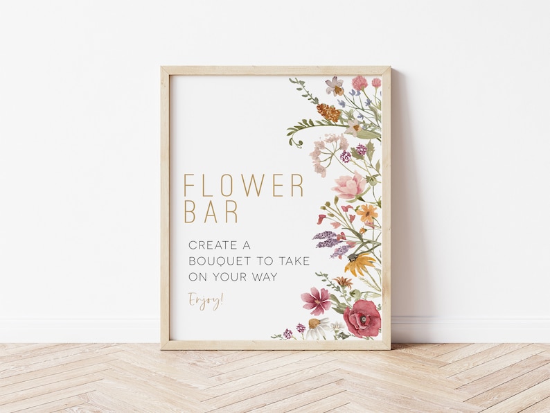 May include: A printable sign with a floral border and the text "FLOWER BAR" in gold lettering. The sign also includes the text "Create a bouquet to take on your way. Enjoy!"