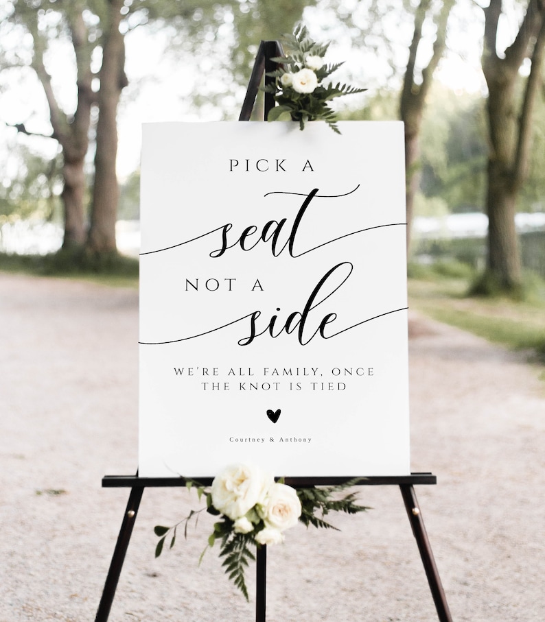 May include: White sign with black calligraphy that reads "Pick a seat, not a side. We're all family, once the knot is tied."  A black heart symbol is below the text, followed by "Courtney & Anthony".