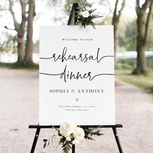 May include: White sign with black text on an easel. The sign reads "Welcome to our rehearsal dinner Sophia & Anthony" with a heart symbol and the date "Saturday, August 15, 2014" and location "Galena, Illinois".