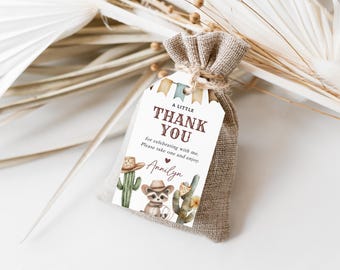 Könnte beinhalten: Ein weißes Dankeschön-Etikett mit einer braunen und weißen Illustration eines Waschbären mit Cowboyhut und Kakteen. Das Etikett lautet "A Little Thank You for celebrating with me. Please take one and enjoy. Annilyn". Das Etikett ist an einem kleinen Jutesack befestigt.