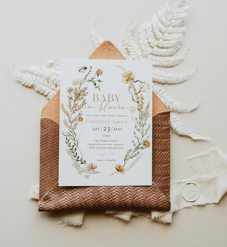 May include: A baby shower invitation featuring a floral wreath design. The invitation reads "Baby in Bloom" and includes the name "Courtney Laura" and the date "Sat 23 May".
