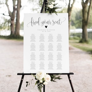 Peut inclure: Un plan de table de mariage blanc sur un chevalet noir, avec les mots "find your seat" en écriture élégante. Le tableau liste les noms sous les numéros de table, avec des accents floraux en haut et en bas. La date "08. 28. 2020" est également affichée.