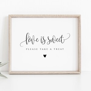Könnte beinhalten: Gerahmter Druck mit den Worten "love is sweet, please take a treat" in eleganter schwarzer Schrift. Unter dem Text befindet sich ein kleines schwarzes Herz. Der Rahmen ist hellbraun und der Hintergrund ist weiß.