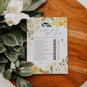 May include: A printable game card with a floral design and a honeycomb pattern. The card has the text "He Said, She Said" and asks players to circle who they think said each statement first, the bride or groom. The card includes 14 statements about relationships and marriage.